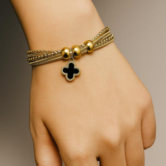Gold bracelet with a black clover charm on a hand against a neutral background