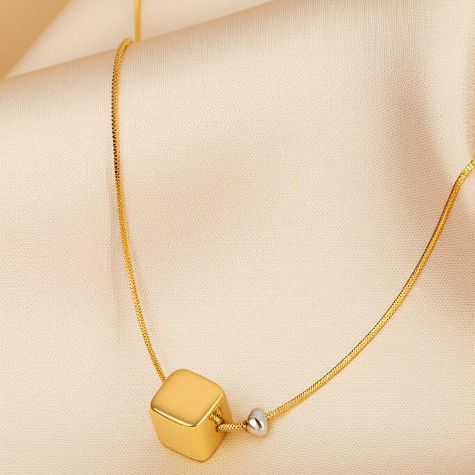 Gold necklace with a cube pendant on a beige fabric background