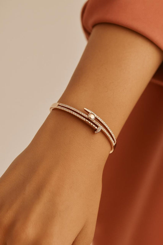 Close-up of a wrist wearing a rose gold bracelet with a pearl on a beige background