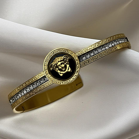 Gold bracelet with black center and diamond accents on a white fabric background